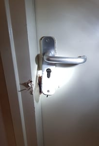 Beschadigde deur met defect deurbeslag en loshangende deurklink.