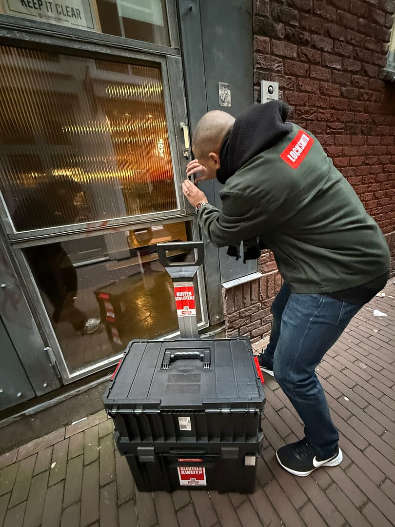 Slotenmaker opent deur met gereedschapskist nabij.