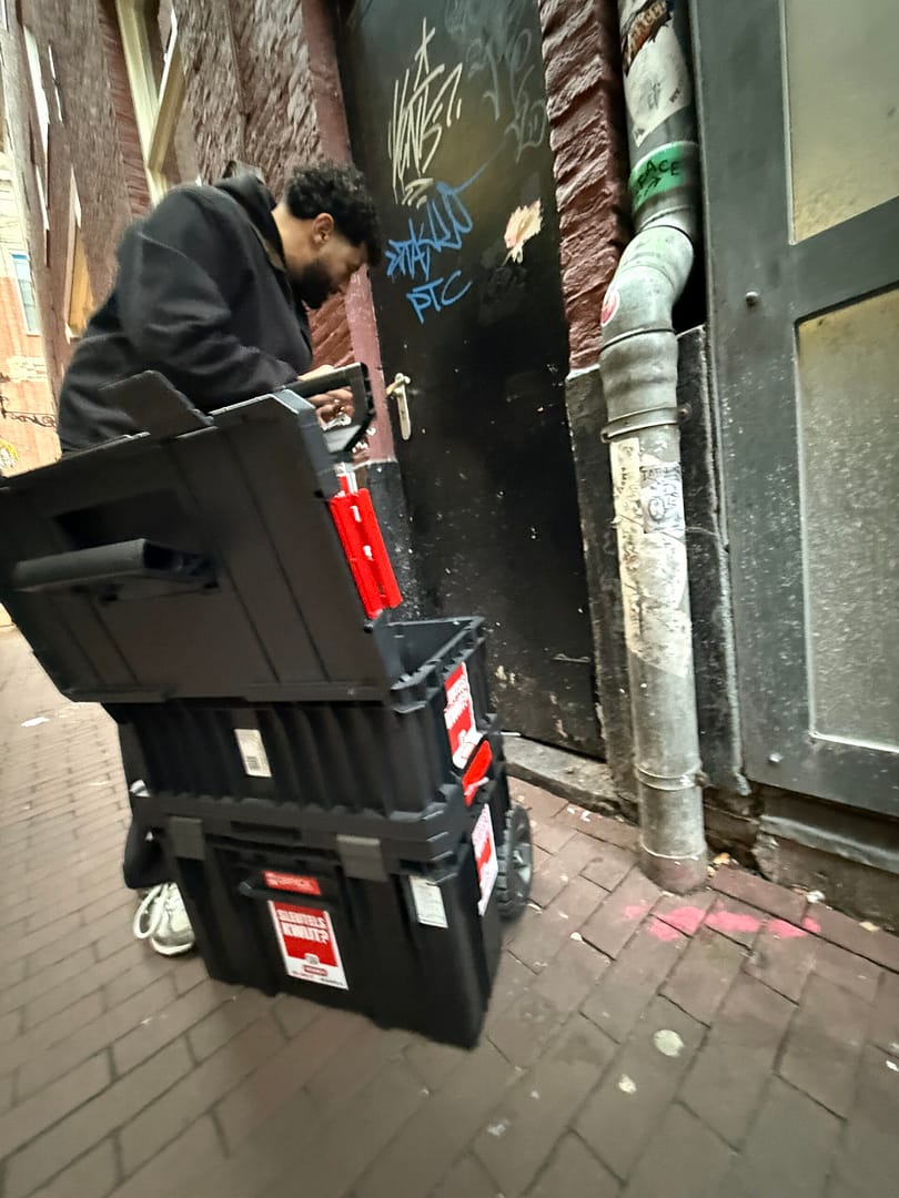 Man verplaatst gereedschapskist in smalle straat.