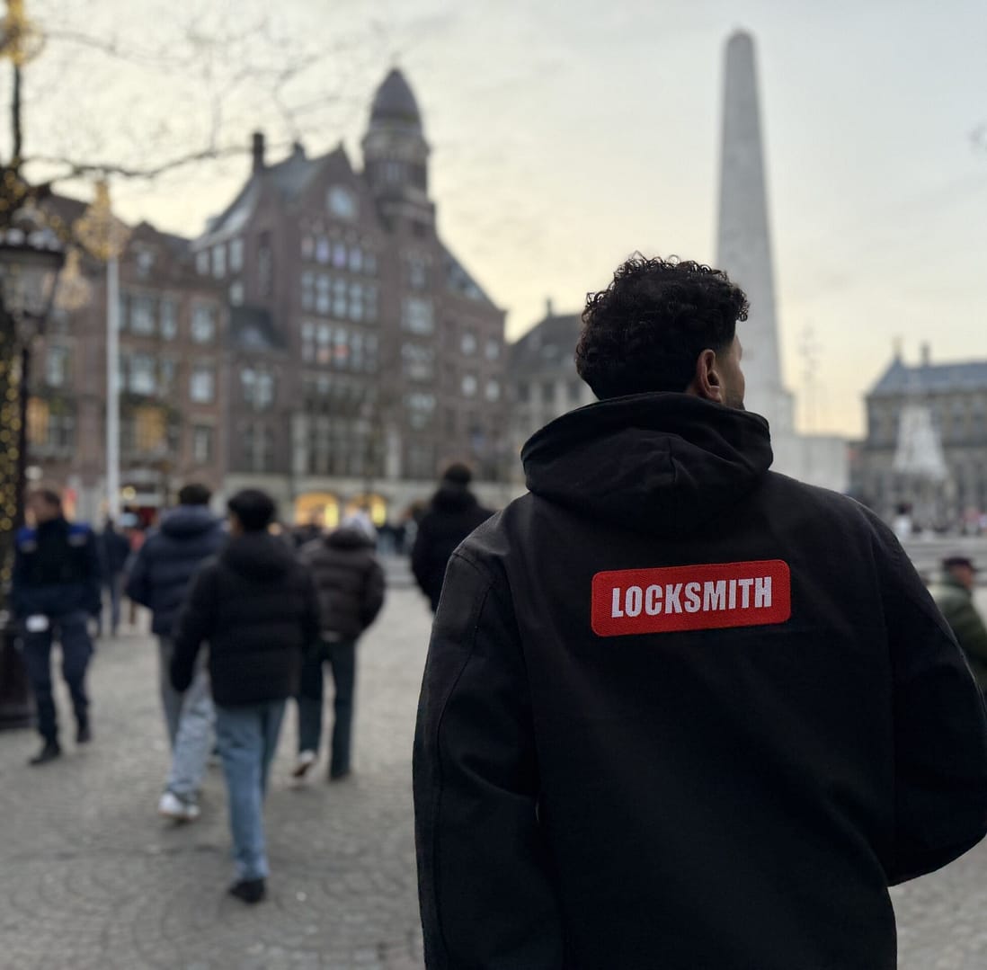 Man in jas met 'Locksmith' op drukke straat.